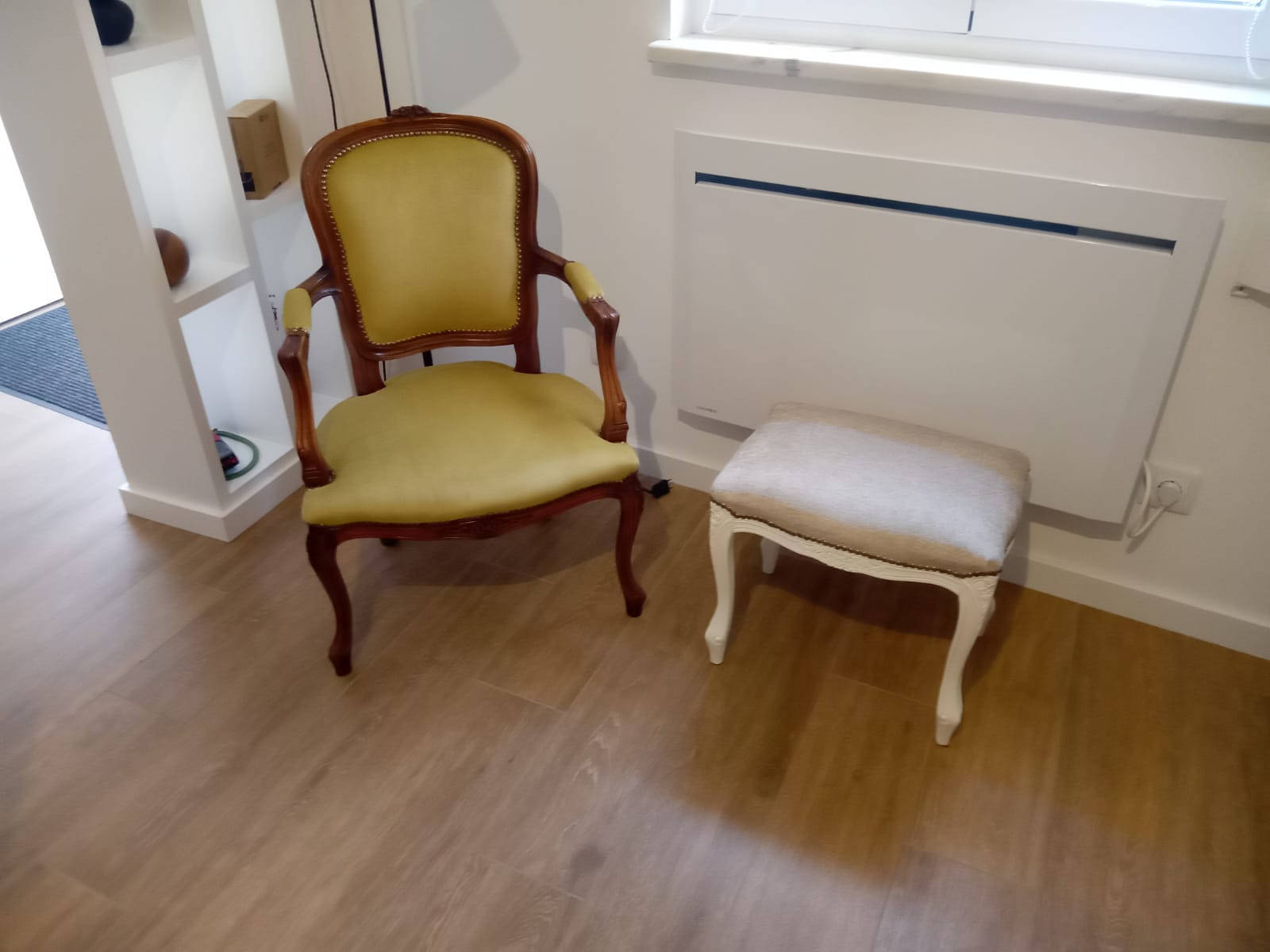 Cadeirão clássico de madeira restaurado, estofado em tecido amarelo, ao lado de uma banqueta branca renovada