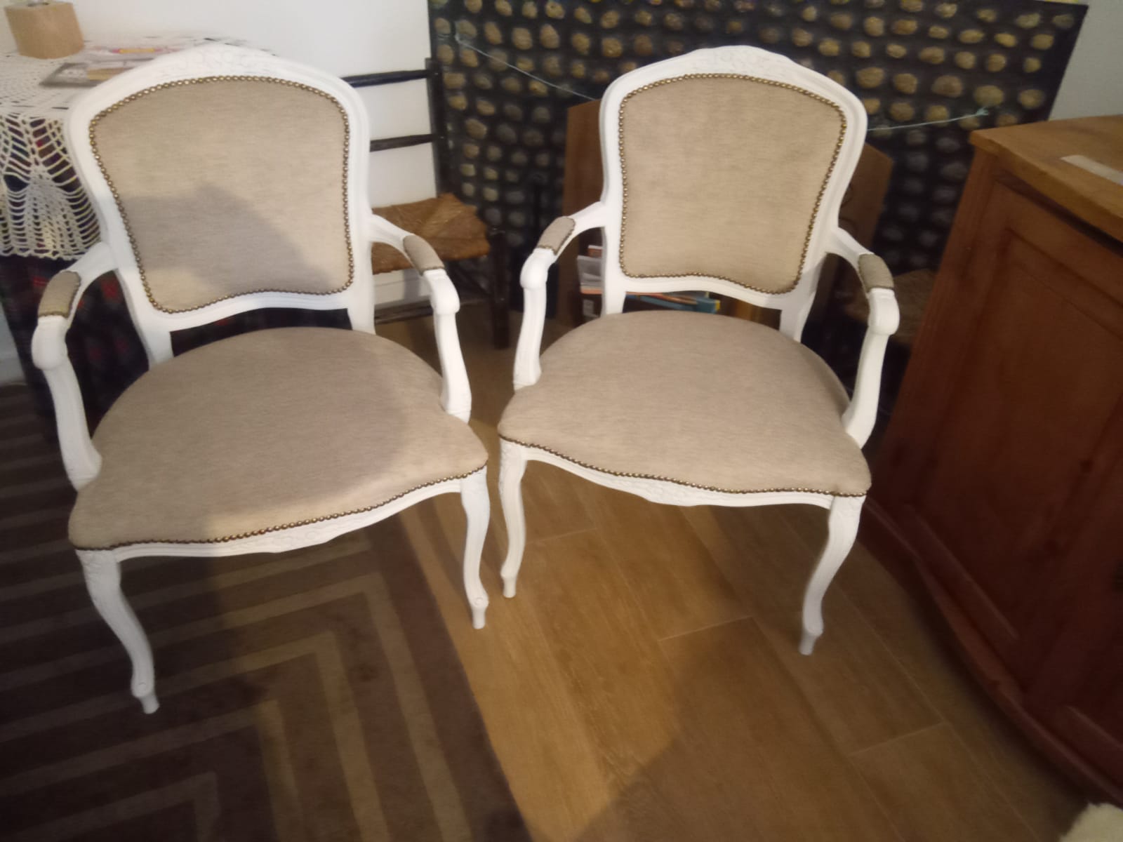 Par de cadeiras de braços clássicas lacadas de branco, estofadas em tecido bege com remate em pregaria dourada